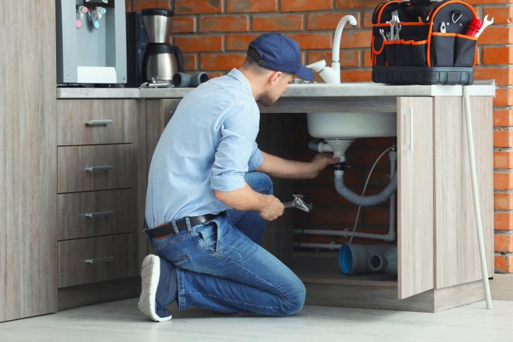 Plumber repairing kitchen sink pipes under the cabinet using tools